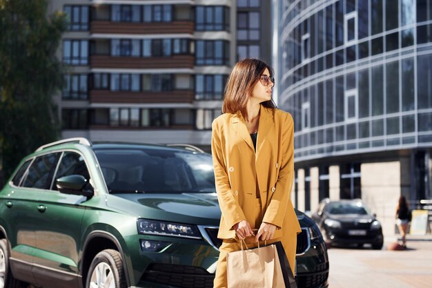 Jeune femme à la mode en manteau de couleur bordeaux pendant la journée avec sa voiture