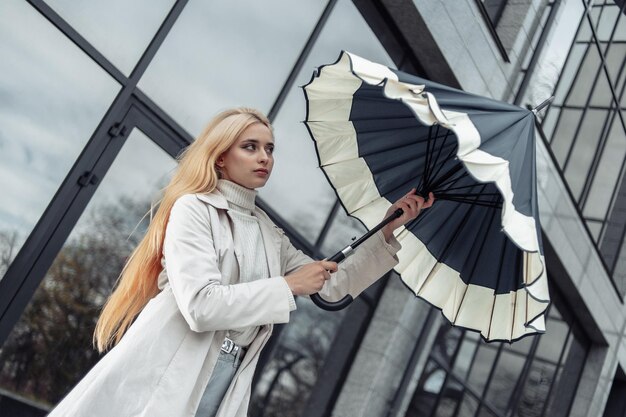 La jeune femme de mode ouvre le parapluie près du centre d'affaires