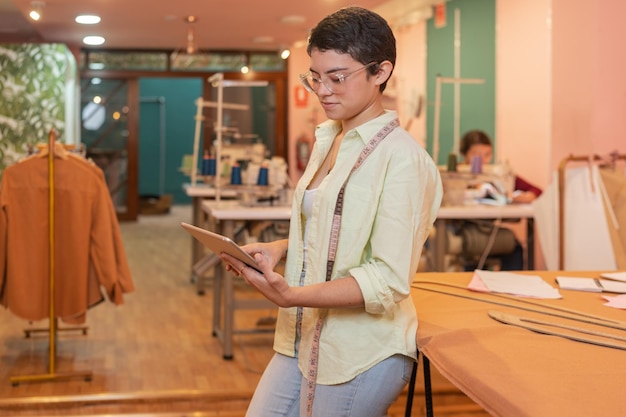 Jeune femme moderne à l'aide d'une tablette numérique tout en travaillant dans un atelier
