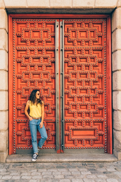 Photo jeune femme moderne avec chemise jaune posant dans une porte rouge à madrid