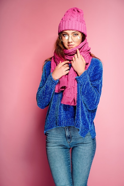 Jeune femme moderne portant un pull bleu et un chapeau rose et une écharpe posant, faisant une drôle d'expression du visage.