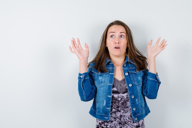 Jeune femme montrant un geste d'abandon en robe, veste en jean et l'air effrayée. vue de face.