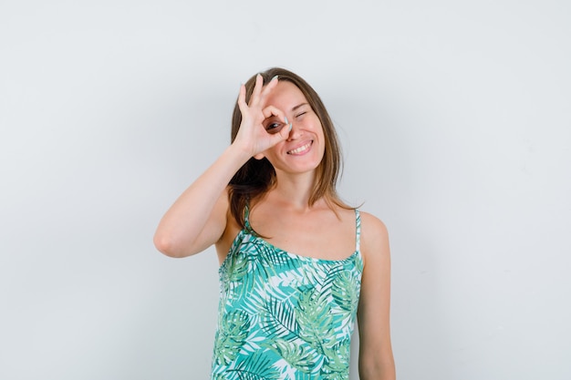 Jeune femme montrant un geste correct en blouse et l'air heureuse, vue de face.