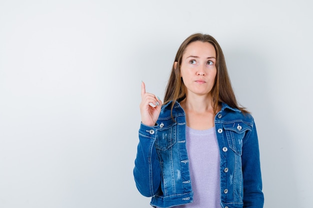 Jeune femme montrant le geste d'eureka, pointant vers le haut, regardant vers le haut en t-shirt, veste et ayant l'air intelligent. vue de face.