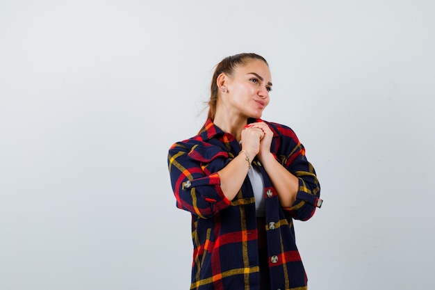 Jeune femme montrant les mains jointes dans un geste suppliant en haut court, chemise à carreaux et l'air paisible. vue de face.