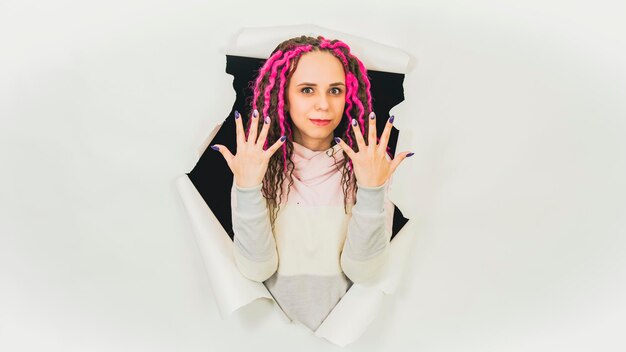 Jeune femme montrant manucure dans le trou de fond blanc Belle femme aux cheveux bouclés montrant ses mains avec des ongles vernis en studio