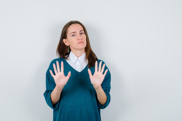 Jeune femme montrant un panneau d'arrêt en pull sur une chemise blanche et à la résolution. vue de face.