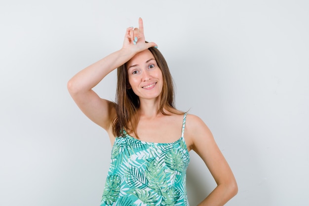 Jeune Femme Montrant Le Signe Du Perdant Sur Le Front Et Semblant Joyeuse, Vue De Face.