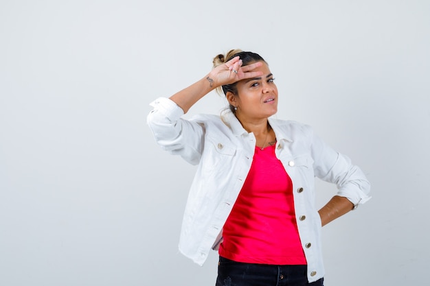 Jeune femme montrant le signe de la victoire en t-shirt, veste blanche et joyeuse, vue de face.