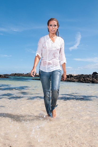 Jeune femme mouillée en vêtements au bord de la mer au printemps ou en été sous un ciel bleu