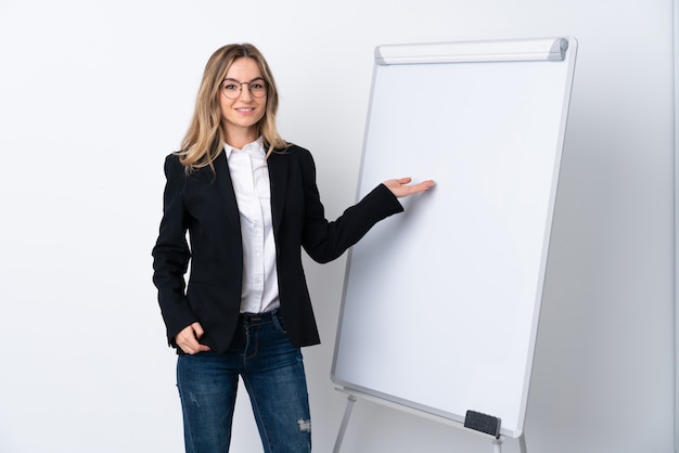 Jeune femme sur un mur blanc isolé donnant une présentation sur tableau blanc et en le pointant