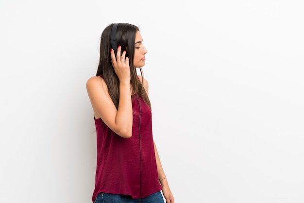 Jeune femme sur un mur blanc isolé, écouter de la musique avec des écouteurs