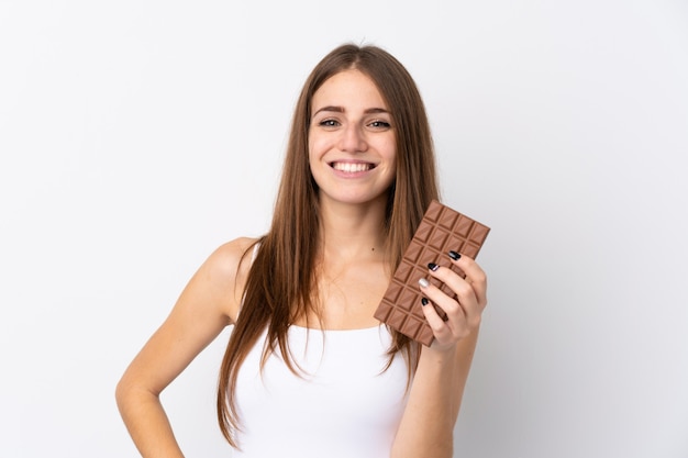 Jeune femme sur un mur blanc isolé en prenant une tablette de chocolat et heureux