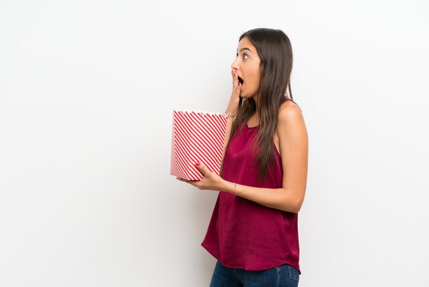 Jeune femme sur un mur blanc isolé, tenant un bol de pop-corn