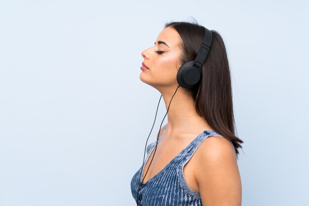 Jeune femme sur un mur bleu isolé, écouter de la musique avec des écouteurs