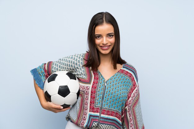 Jeune femme sur un mur bleu isolé, tenant un ballon de foot