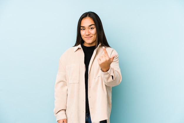 Jeune femme sur un mur bleu pointant du doigt vers vous comme pour vous inviter à vous rapprocher.