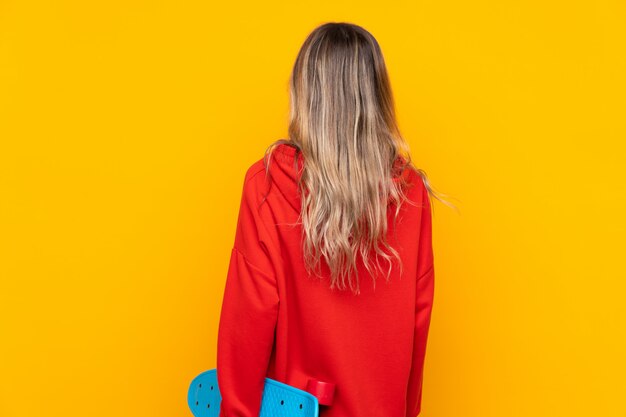 Jeune femme sur un mur jaune isolé avec un patin en position arrière