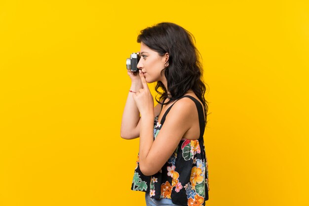 Jeune femme sur un mur jaune isolé, tenant une caméra