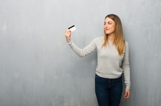 Jeune femme sur un mur texturé détenant une carte de crédit et de penser