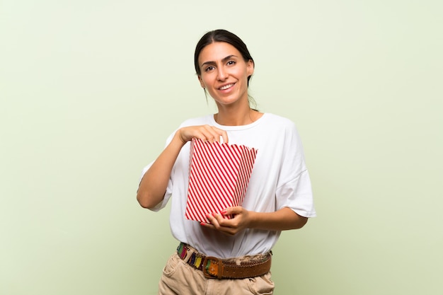 Jeune femme sur un mur vert isolé, tenant un bol de pop-corn