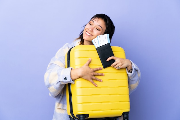 Jeune femme sur mur violet en vacances avec valise et passeport