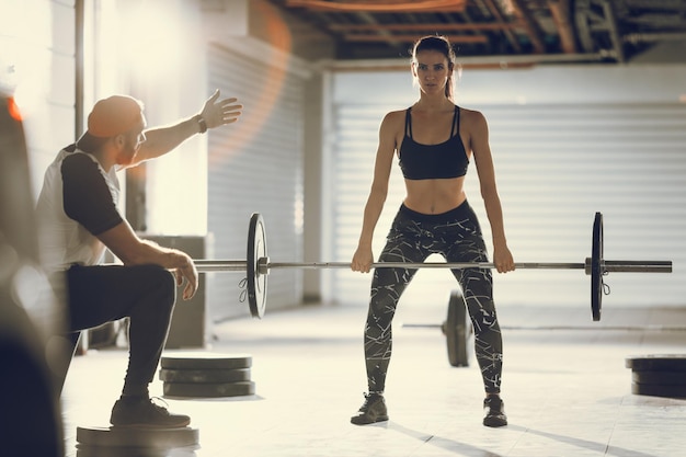 Jeune femme musclée faisant de l'exercice avec un entraîneur personnel à la salle de gym du garage.