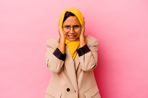 Jeune femme musulmane d'affaires isolée sur fond rose couvrant les oreilles avec les mains essayant de ne pas entendre un son trop fort.