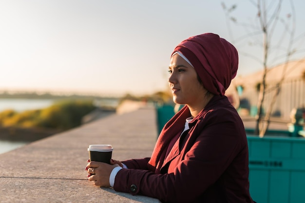 Jeune femme musulmane arabe en hijab debout au bord de la rue et buvant du café à emporter copier l'espace et le lieu pour la publicité