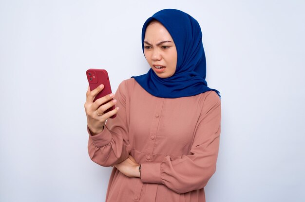 Jeune femme musulmane asiatique en colère en chemise rose à l'aide de téléphone portable isolé sur fond blanc Concept de style de vie religieux des gens