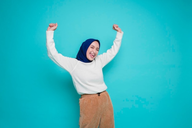 Une jeune femme musulmane asiatique avec une expression heureuse et réussie portant une chemise blanche et un hijab isolé sur fond blanc