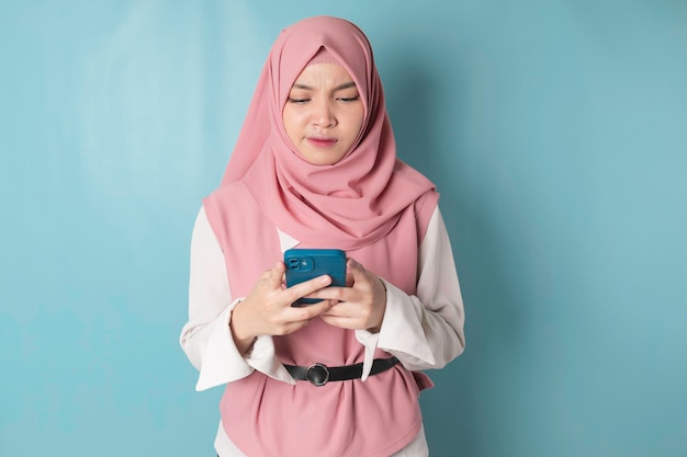 Jeune femme musulmane asiatique en hijab rose se sentant sérieuse et se concentrant en tenant le smartphone à la main