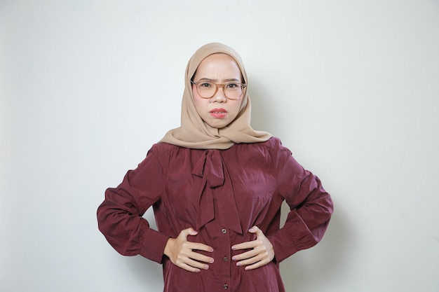 Jeune femme musulmane asiatique portant des lunettes tristes tenant le ventre à deux mains