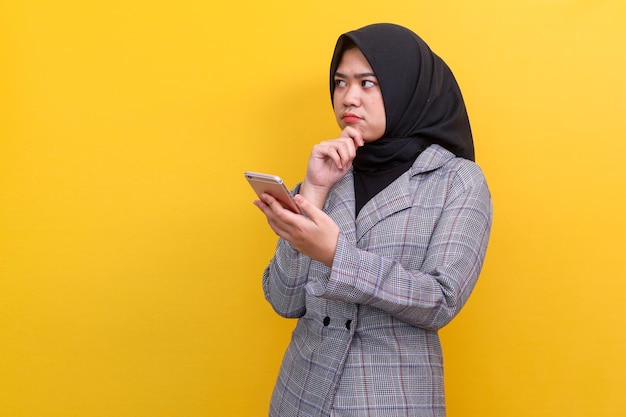 Jeune femme musulmane asiatique réfléchie pensant à quelque chose tout en tenant un téléphone portable