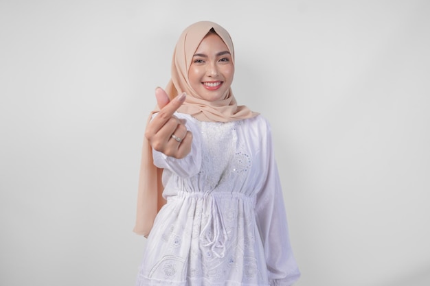 Jeune femme musulmane asiatique en robe blanche et hijab faisant un geste de forme d'amour de cœur avec les mains dans diverses poses isolées sur un fond blanc
