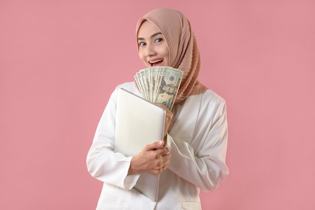 Jeune femme musulmane détient de l'argent et un ordinateur portable sur fond isolé