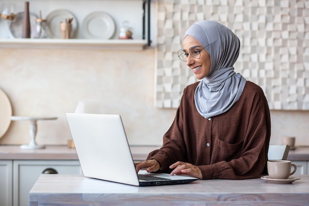 Jeune femme musulmane en développeur programmeur hijab travaillant à la maison assis dans la cuisine à l'ordinateur portable