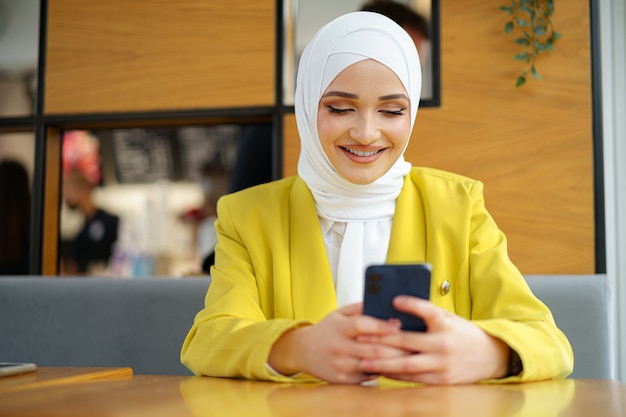 Jeune femme musulmane en hijab à l'aide de son smartphone au café