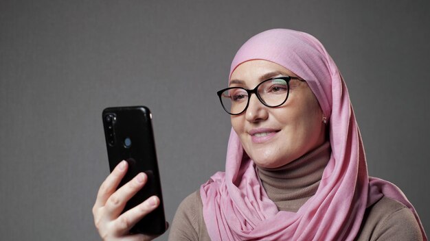 Une jeune femme musulmane en hijab sourit en regardant un spectacle à l'aide d'un téléphone