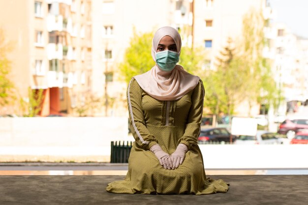 Jeune femme musulmane priant à l'extérieur portant un masque de protection et des gants