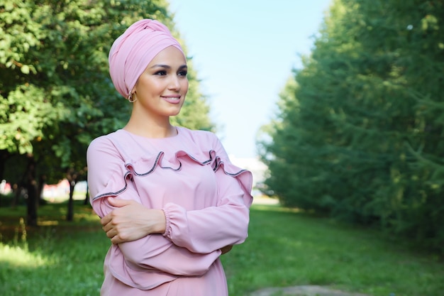 Jeune femme musulmane en robe rose et turban sur fond d'arbres verts, espace de copie.