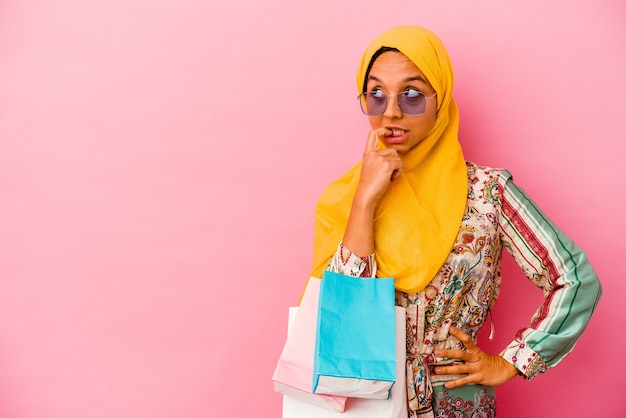 Photo jeune femme musulmane shopping des vêtements isolés sur fond rose détendue en pensant à quelque chose en regardant un espace de copie.