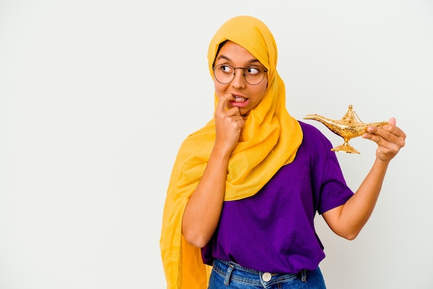 Jeune femme musulmane tenant une lampe isolée sur fond blanc détendu penser à quelque chose en regardant un espace de copie.