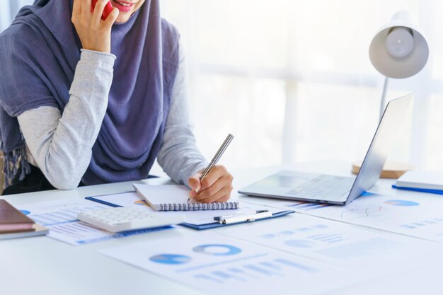 Une jeune femme musulmane travaillant dans un bureau d'affaires portant le hijab travaille comme projet de démarrage de PME en utilisant un appel téléphonique un téléphone