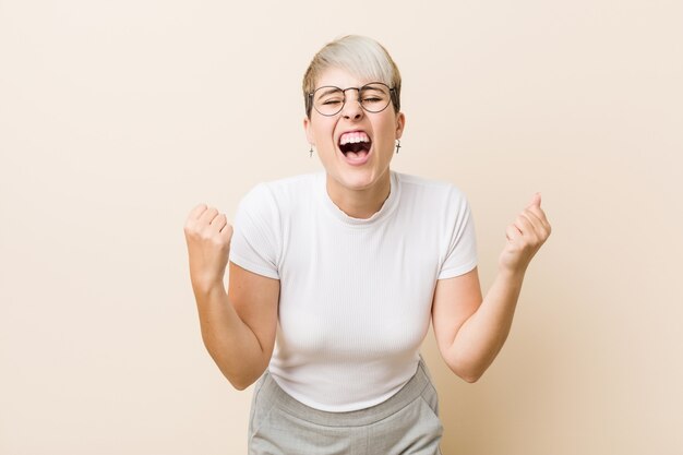 Jeune femme naturelle authentique portant une chemise blanche acclamant insouciante et excitée. Concept de victoire.