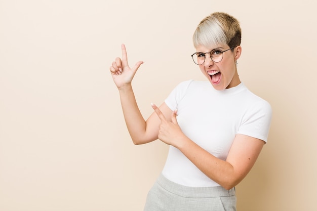 Jeune femme naturelle authentique portant une chemise blanche pointant avec des index vers un espace de copie, exprimant l'excitation et le désir.