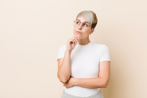 Jeune femme naturelle authentique vêtue d'une chemise blanche à la recherche de côté avec une expression sceptique et sceptique