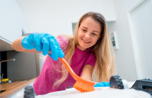 Une jeune femme nettoie un aspirateur robot de la saleté après le nettoyage
