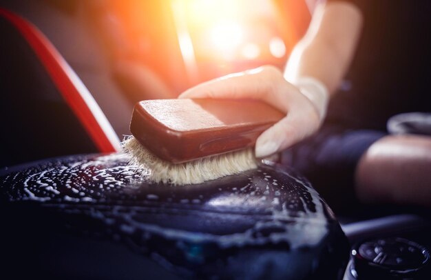 Jeune femme nettoyant l'intérieur de la voiture à l'aide d'une brosse spéciale avec de la mousse