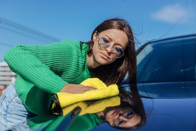 Une jeune femme nettoyant et polissant sa voiture avec un chiffon en microfibre jaune Concept de voiture en prenant soin